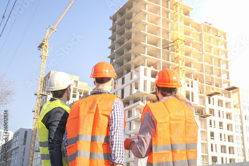 male workers engineers at a construction site with the head in helmets look at the house that is being built