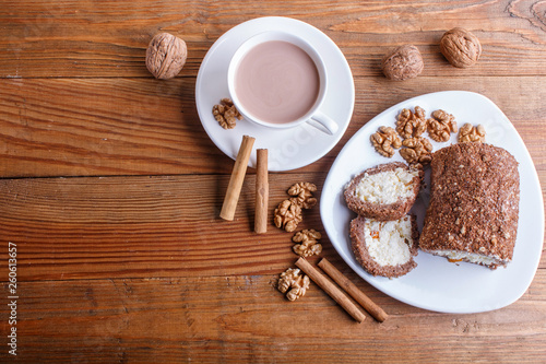 Roll cake with curd and walnuts isolated on brown wooden background...