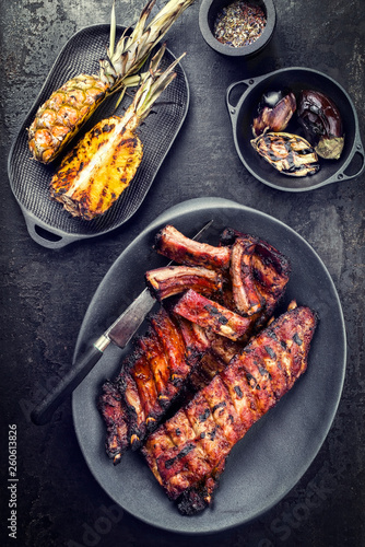 Barbecue spare ribs St Louis cut hot honey chili marinade with pineapples and eggplant as top view on a modern design cast iron pan