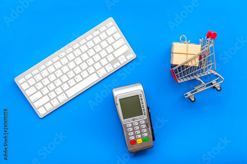 Online shopping concept with trolley near card machine, keyboard on blue background top view