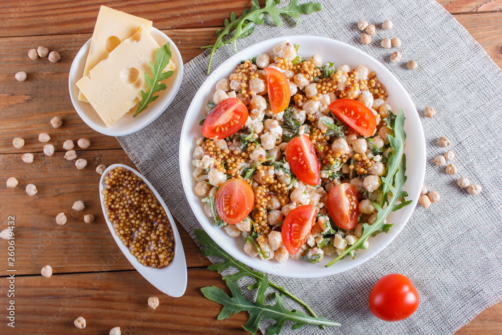 Vegetarian salad of boiled chickpeas, cheese, arugula, mustard and cherry tomatoes on brown wooden background. Vegetarian salad of boiled chickpeas, cheese, arugula, mustard and cherry tomatoes on brown wooden background.
