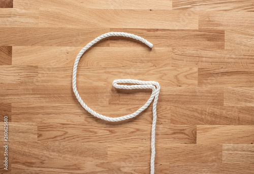 The letter G formed with white rope on a wooden table