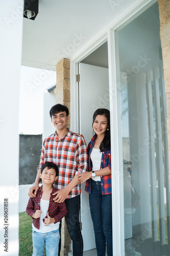 young asian family in front of the door of their house looking at camera and smiling