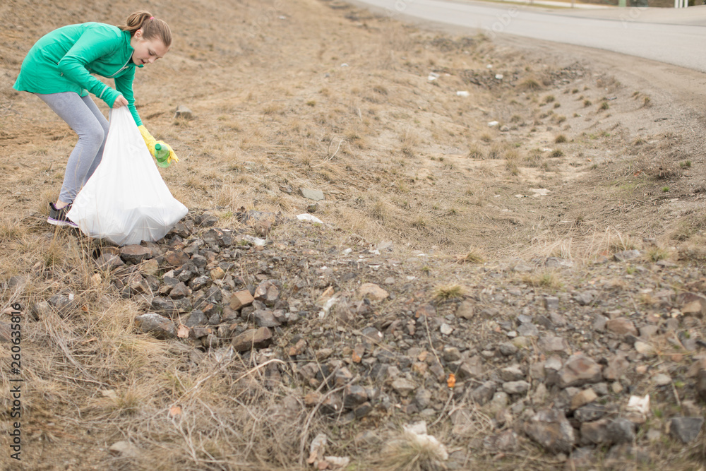 Fototapeta premium Young girl picking up litter on side of road with garbage bag