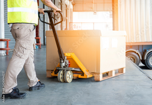 Workers Using Hand Pallet Jack Unloading Package Boxes into Cargo Container. Delivery Shipment Boxes. Trucks Loading at Dock Warehouse. Supply Chain. Warehouse Shipping Transport and Logistics.