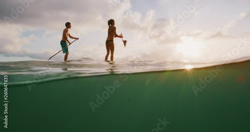 Over under shot of young happy active couple stand up paddling together at sunset in the ocean, island beach ocean lifestyle, active healthy life