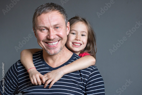 Little daughter hugs dad by the neck from behind