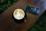 Cup of coffee with beautiful Latte art on wood bar table beside a cellphone