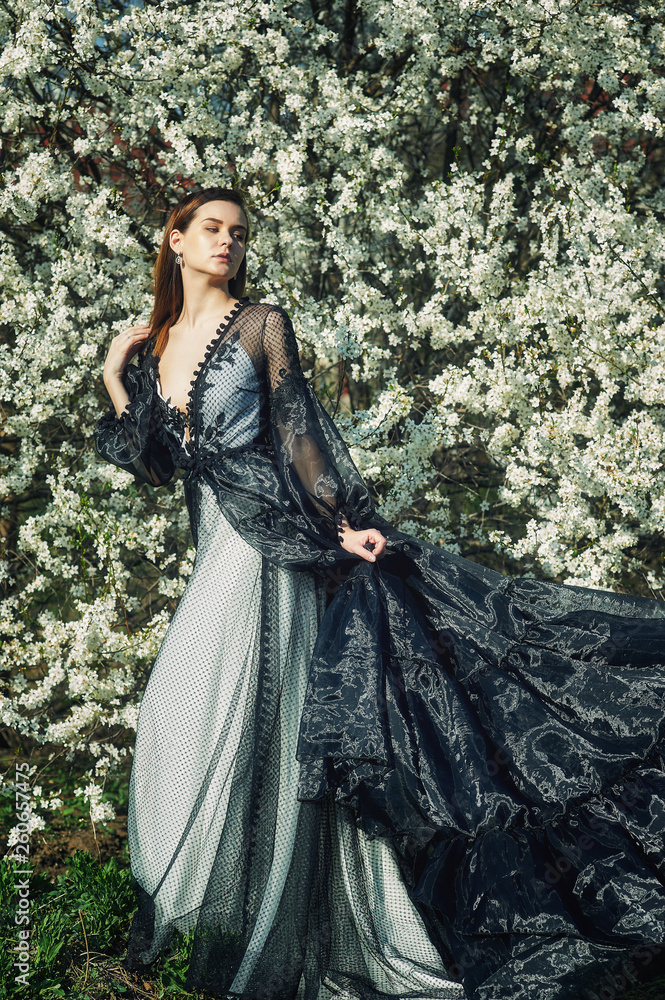 Portrait of a young beautiful fashionable woman in an evening dress . Girl posing in a blooming garden Portrait of a young beautiful fashionable woman in an evening dress . Girl posing in a blooming garden
