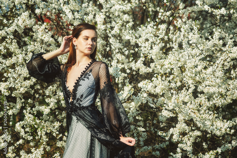 Obraz premium Portrait of a young beautiful fashionable woman in an evening dress . Girl posing in a blooming garden
