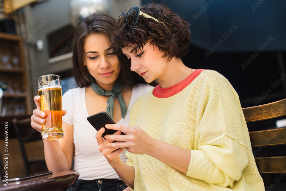Two girls chatting while having a beer. Long haired and short haired girl drinking beer. 