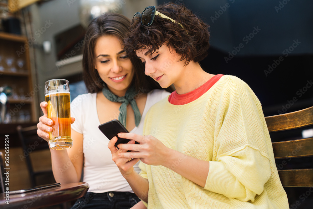 Two girls chatting while having a beer. Long haired and short haired girl drinking beer. 