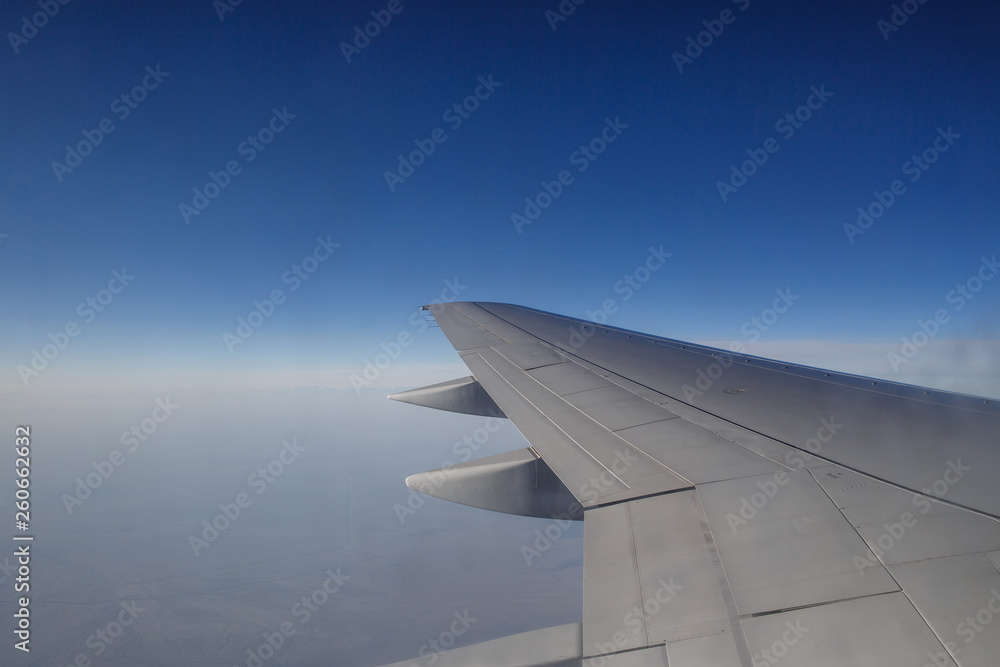 Fototapeta premium Wing of an airplane flying above the morning clouds