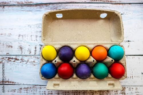 Ten colorful bright easter eggs in carton egg box on wooden table background