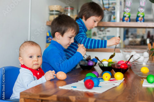 Three children, brothers, coloring and painting easter eggs at home in kitchen