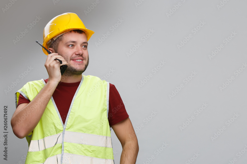 Image of cheerful builder in yellow helmet talking on radio in studio.