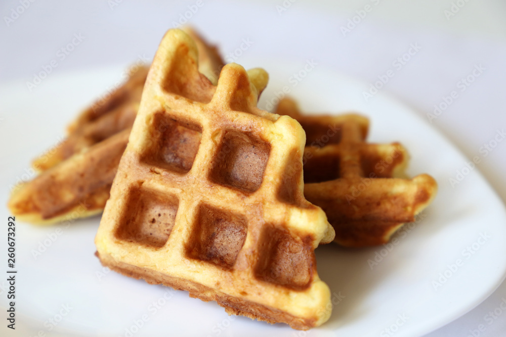 Belgian waffles in white plate. Healthy breakfast close up, pieces of freshly baked classic wafer Belgian waffles in white plate. Healthy breakfast close up, pieces of freshly baked classic wafer