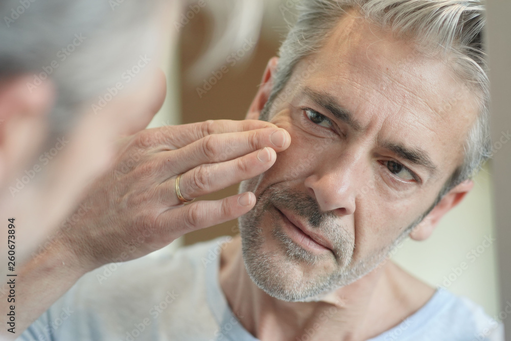 Obraz premium Portrait of mature handsome man looking in mirror at home