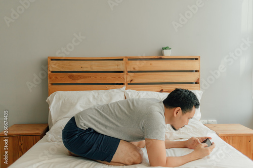 Man is playing mobile game with his smartphone on the bed.