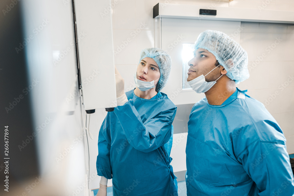 good-looking and beautiful doctors in uniforms and medical masks looking at screen good-looking and beautiful doctors in uniforms and medical masks looking at screen