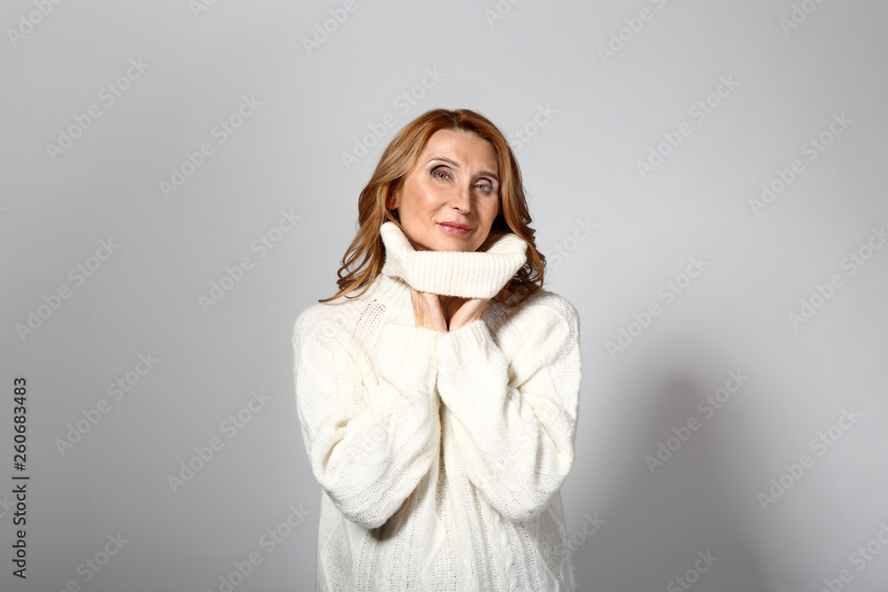 Mature woman in warm sweater on grey background Mature woman in warm sweater on grey background