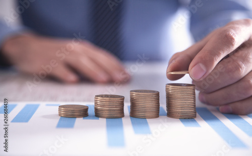 Businessman stacking coins with financial graphs on the desk.