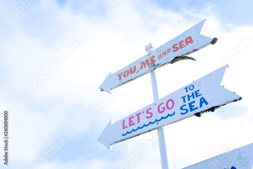 Wooden vintage white guide post signpost direction to the sea in sunny daylight with white cloud sky background