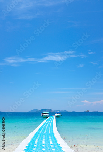 Plastic floating walkway bridge and pier on blue sea water in tropical island under bright blue sky in sunny day  © Putthipong