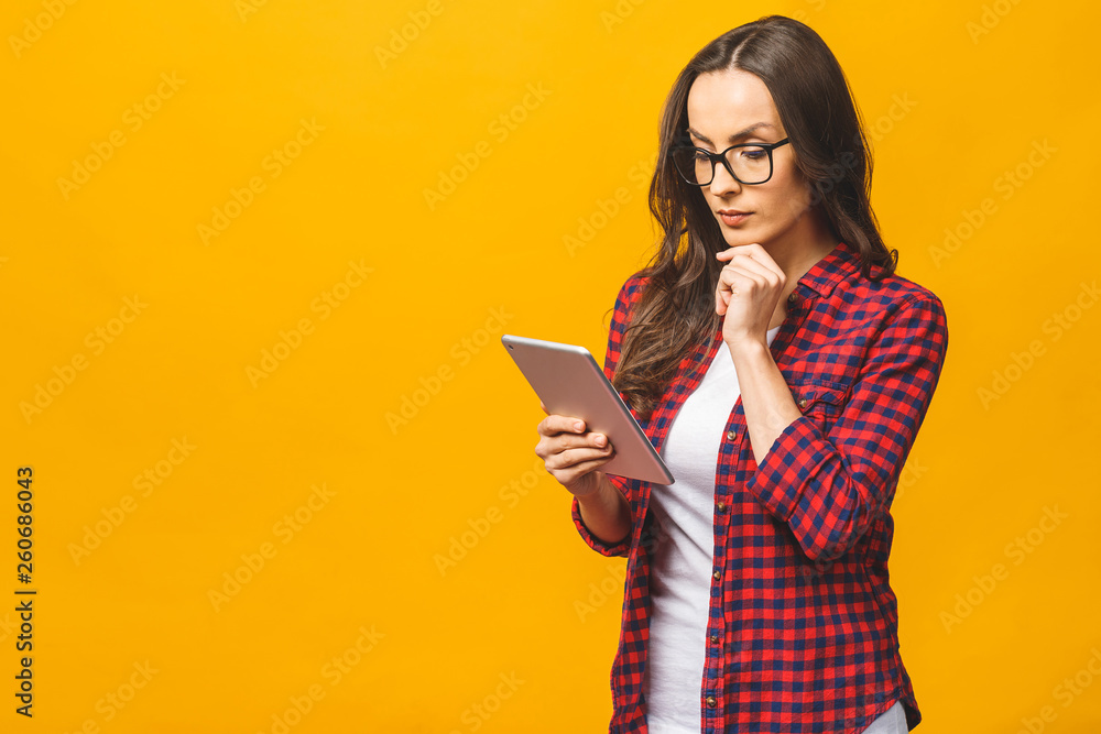 Portrait with copy space empty place of pretty charming confident smiling woman in casual having tablet in hands isolated against yellow background. Portrait with copy space empty place of pretty charming confident smiling woman in casual having tablet in hands isolated against yellow background.
