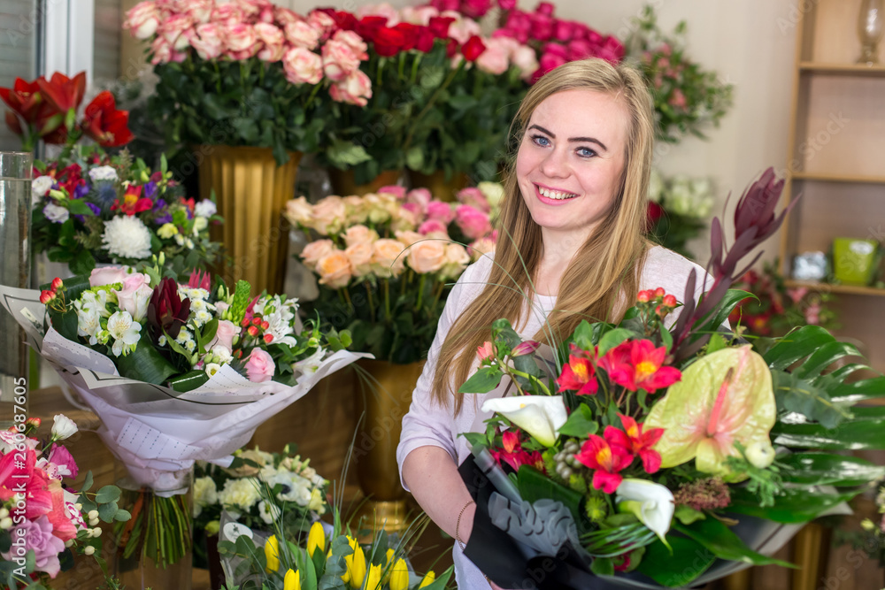 Young happy florist woman holding a beautiful flower bouquet  in a floral boutique. Looking at camera, smiling.