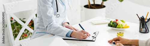 panoramic shot of nutritionist writing diagnosis near patient photo