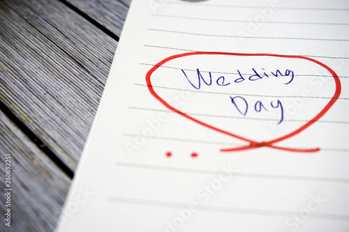 The words "wedding day" means happiness written on a white papernote to remind you an event in that day with white wooden as a background