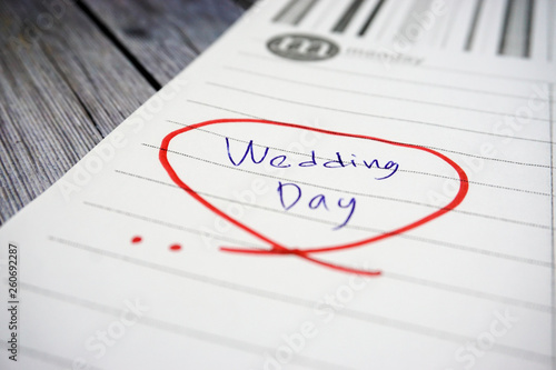 The words "wedding day" means happiness written on a white papernote to remind you an event in that day with white wooden as a background