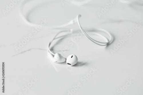 selective focus of white wired earphones on white surface with copy space