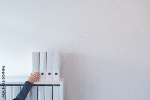 Hand reaching for document ring binder on office shelf