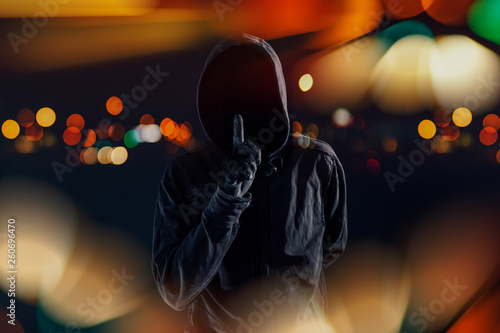 Foto Hooded maniac with finger on lips gesturing shh sign