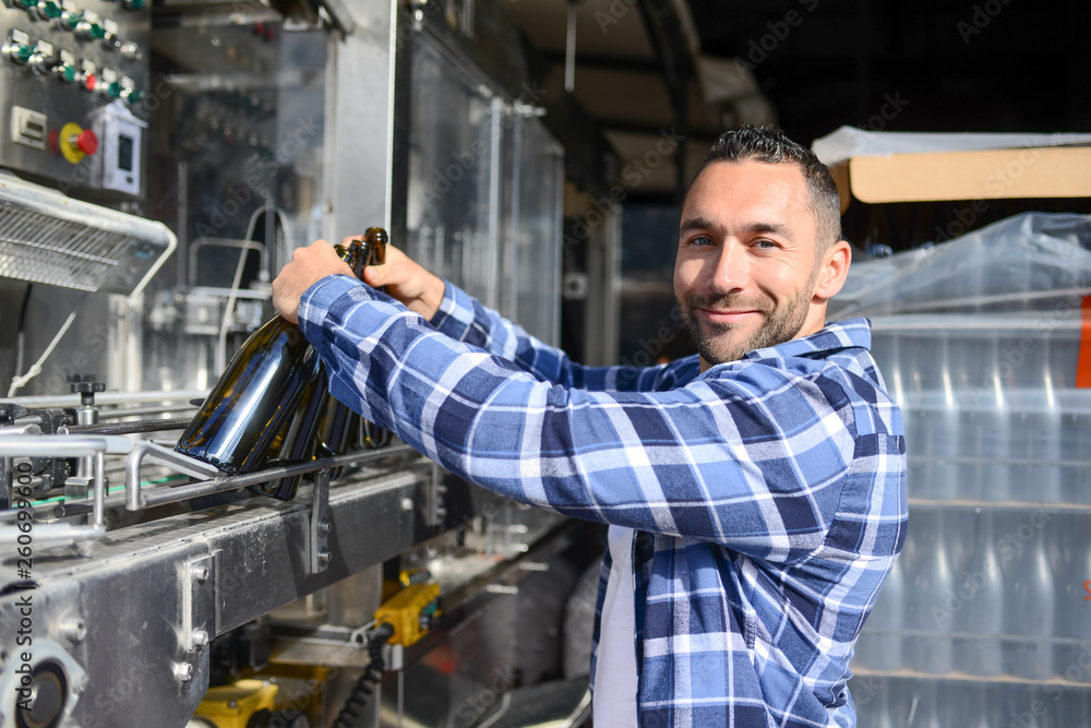 young man wine maker working filling wine bottle with automatic bottling machine young man wine maker working filling wine bottle with automatic bottling machine