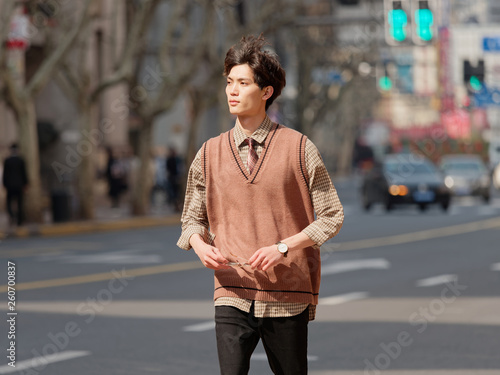 Portrait of a handsome Chinese young man with Korean style clothes walking on street in hurry in sunny day, male fashion, cool Asian young man lifestyle.