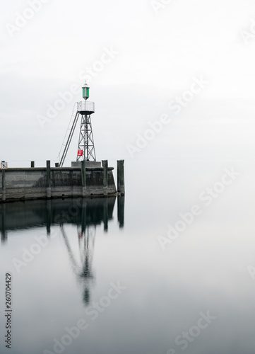 signal light and harbor wall on calm lake waters under an overcast sky negative space abstract