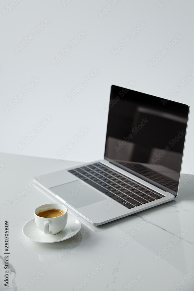 selective focus of laptop with blank screen and coffee cup isolated on grey selective focus of laptop with blank screen and coffee cup isolated on grey
