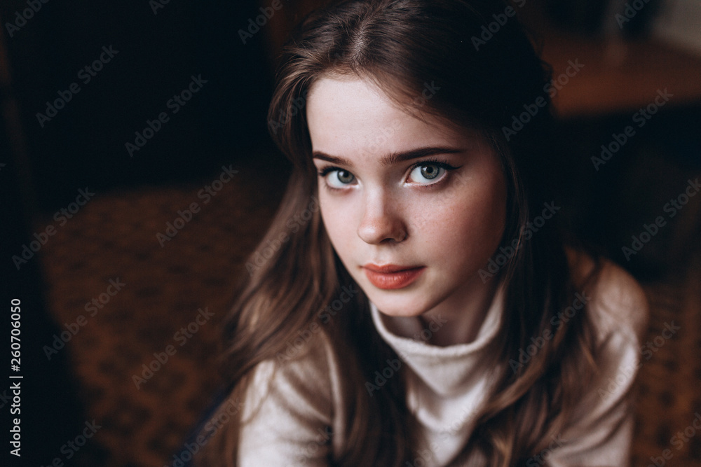 Fototapeta premium Cheerful young girl's portrait having breakfast at cozy home with big cup of coffee or tea holding in hands sitting near window and dreaming. Lifestyle, relaxation, natural beauty, teenage age concept