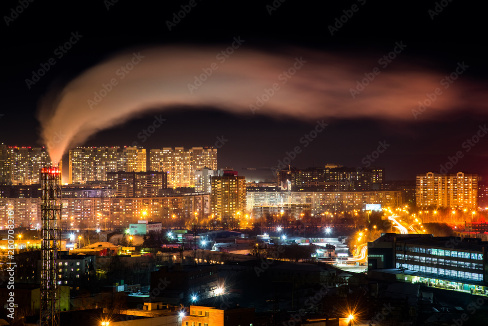 Telephoto lens long exposure shot of night cityscape with pipe and chimney emitting steam or smoke