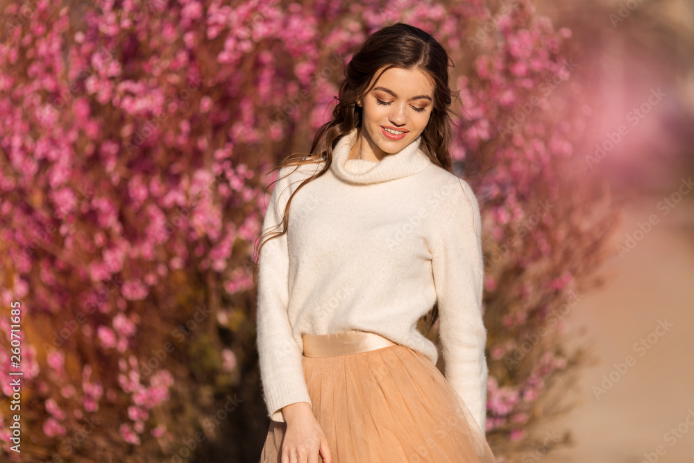 Happy beautiful teen girl with perfect skin and makeup is wearing romantic clothes posing near blossom tree in cherry garden Happy beautiful teen girl with perfect skin and makeup is wearing romantic clothes posing near blossom tree in cherry garden