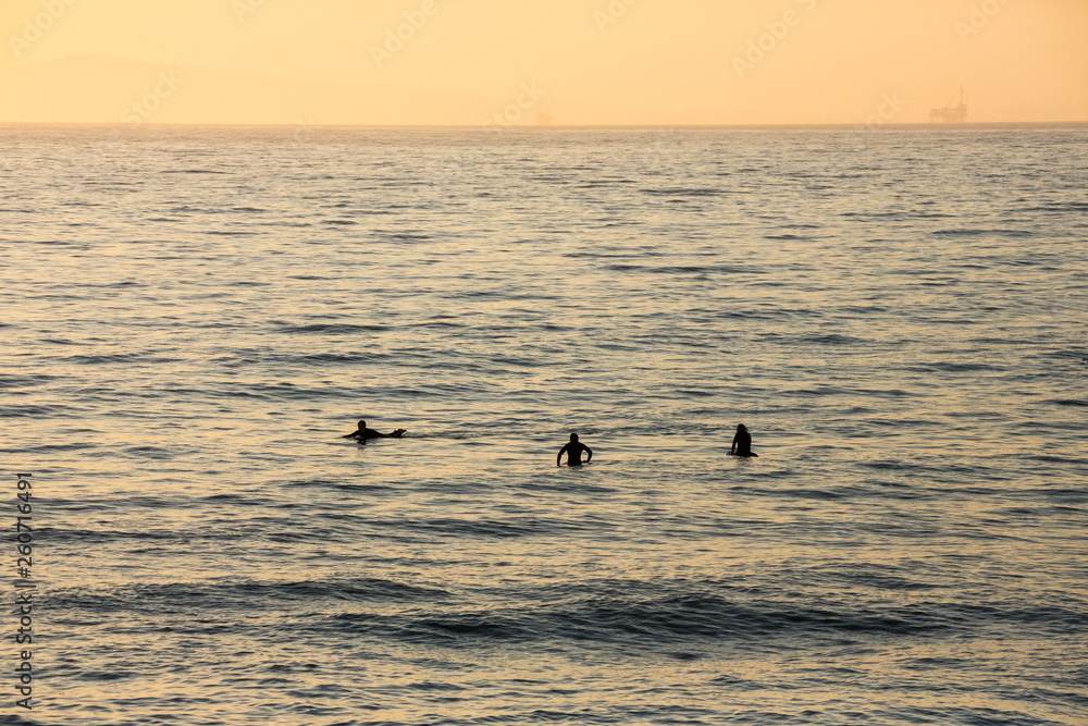 Surfer silhouettes waiting for the perfect wave at sunset Surfer silhouettes waiting for the perfect wave at sunset