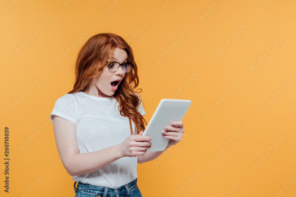 surprised redhead girl using digital tablet isolated on yellow with copy space surprised redhead girl using digital tablet isolated on yellow with copy space