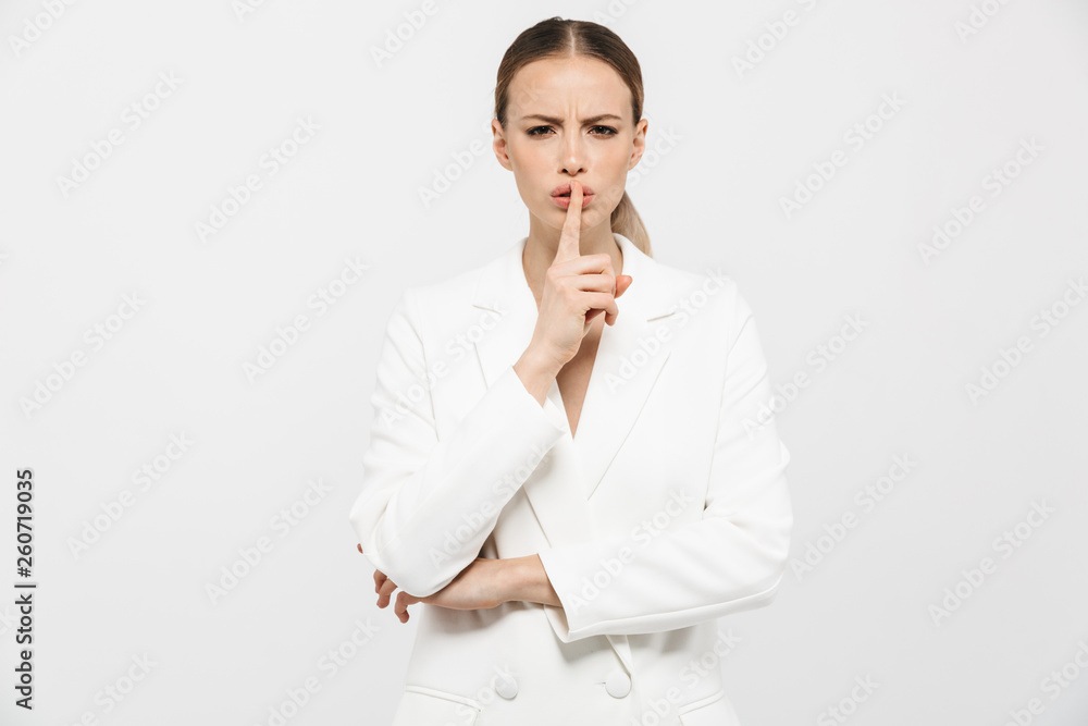 Photo of european businesswoman holding index finger on lips with strict look isolated over white background Photo of european businesswoman holding index finger on lips with strict look isolated over white background