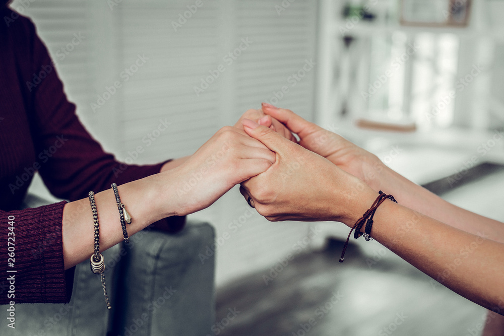 Supportive psychologist wearing bracelets shaking hands of client
