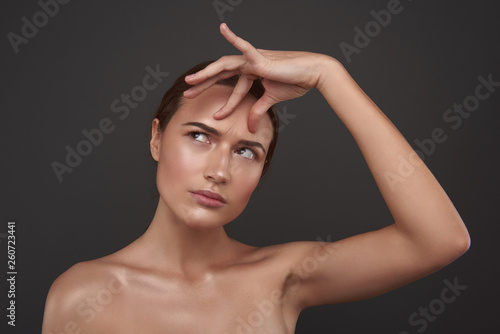 Fototapeta Beautiful young woman touching skin on her forehead and looking away