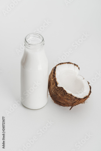 organic vegan coconut milk in bottle near coconut half on grey background
