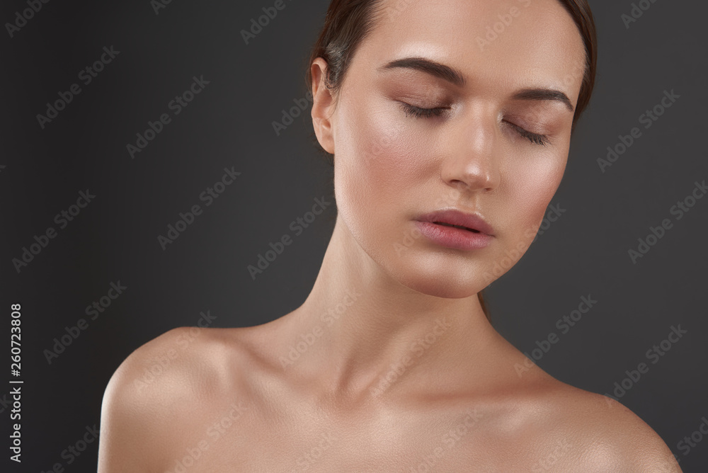 Charming young woman with closed eyes standing against gray background Charming young woman with closed eyes standing against gray background